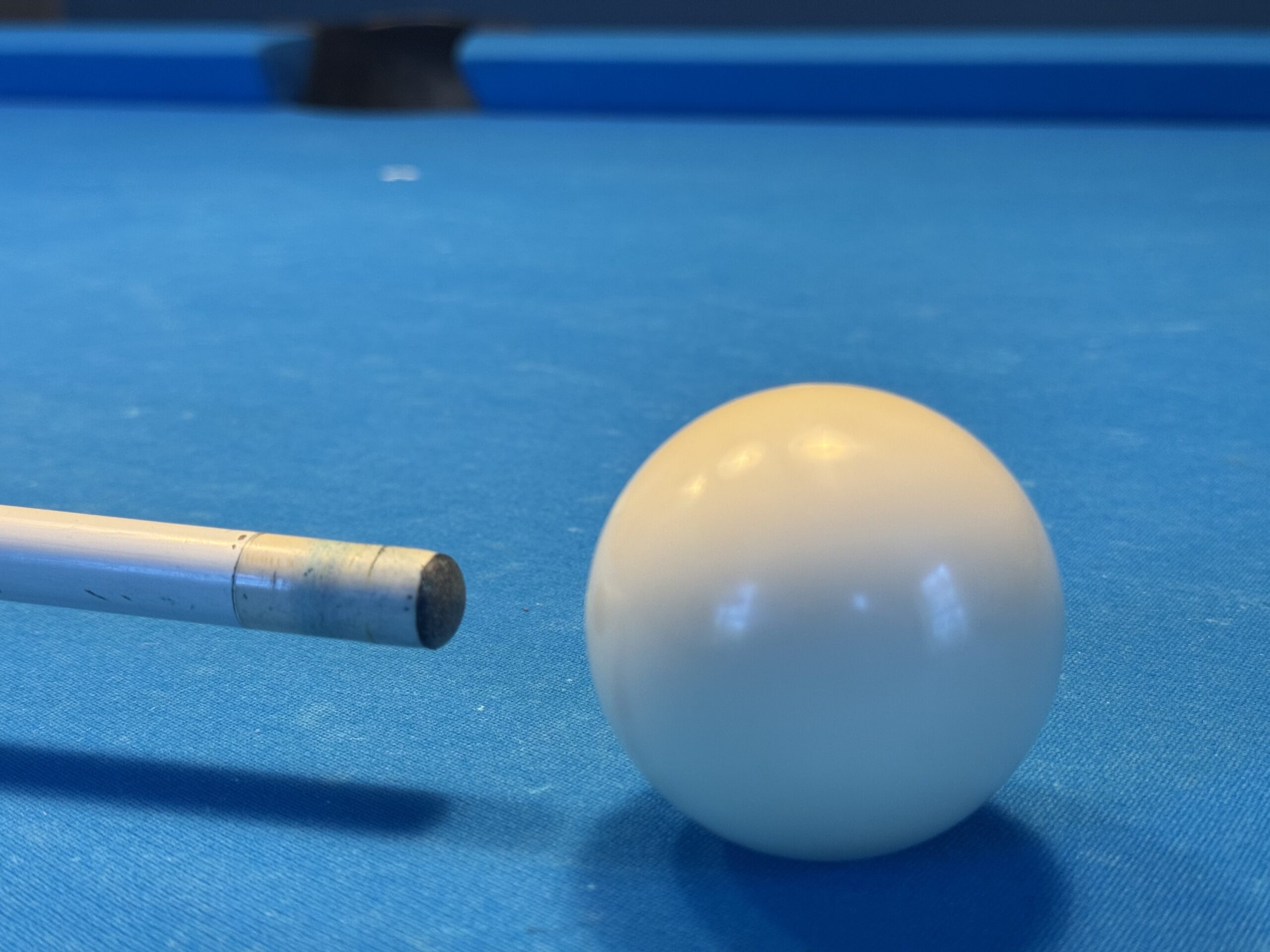 Worn pool cue tip striking a cue ball, showing flattened leather and miscue risk